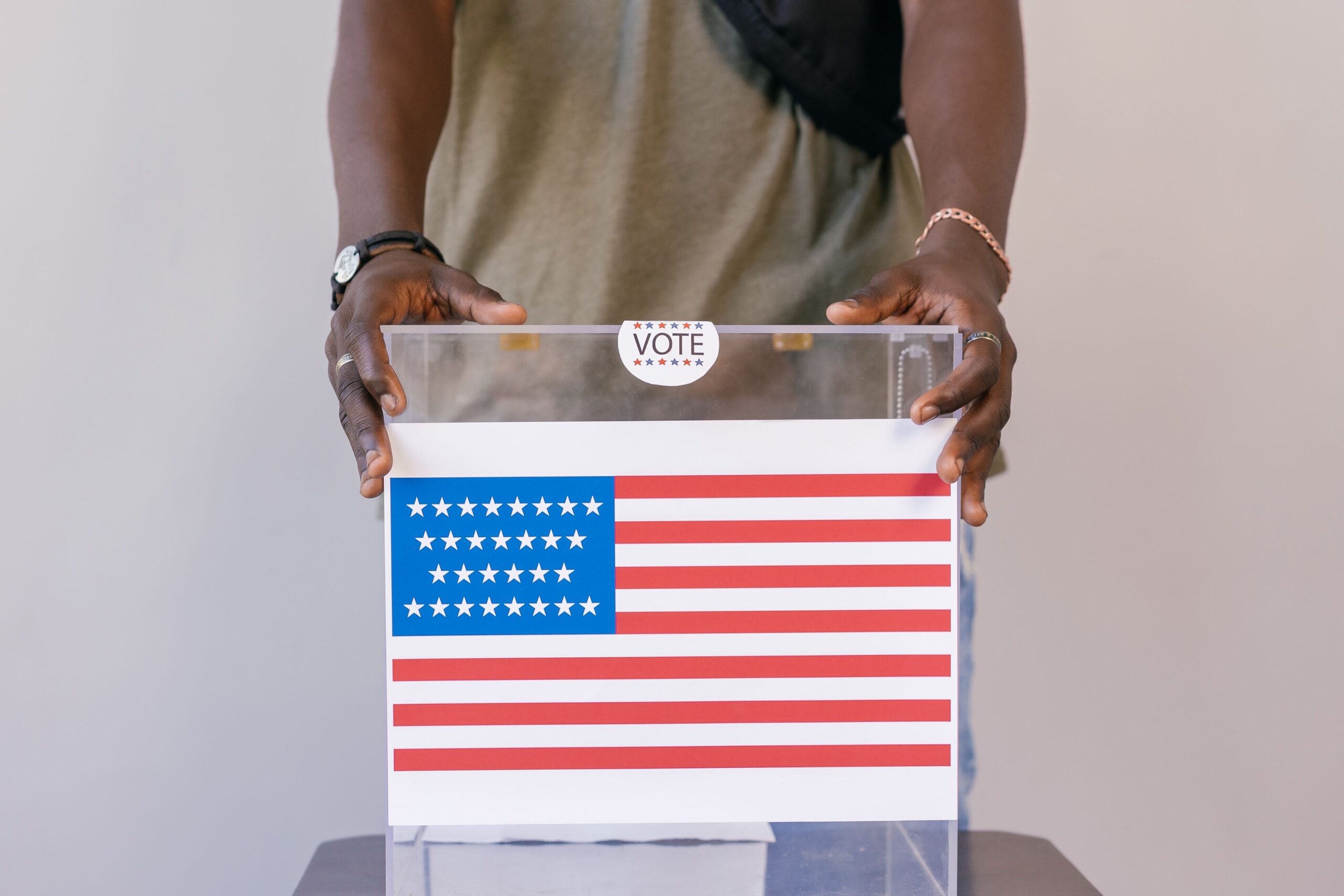 Photo depecting politics: a man holding a podium that has the american flag and a voting sticker pasted on the front